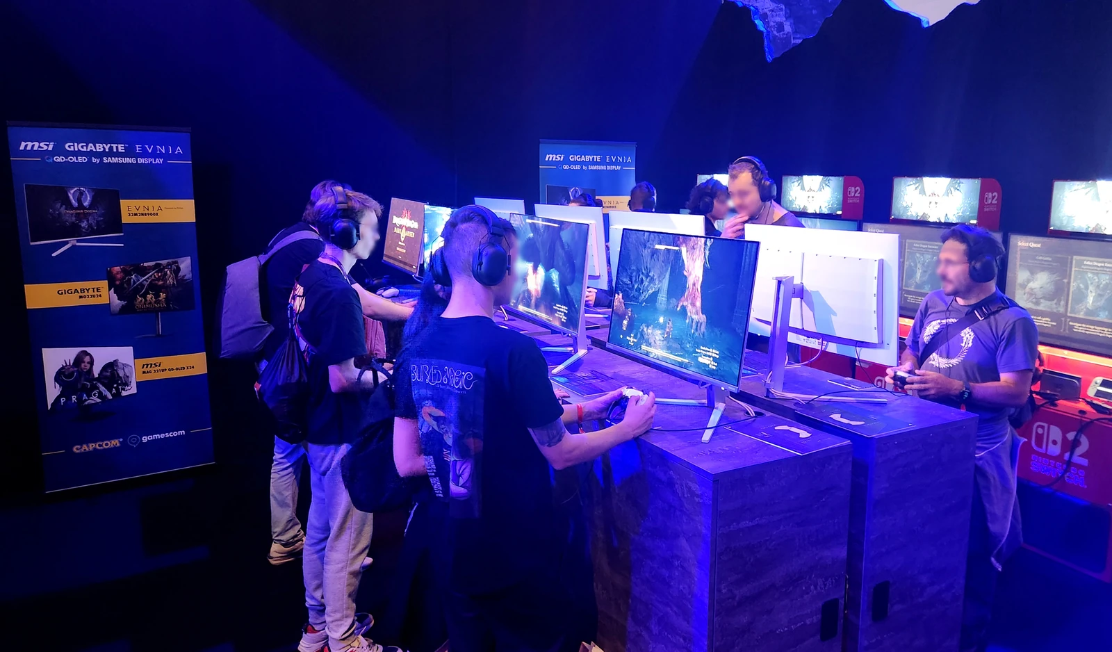 Visitors playing on QD-OLED gaming monitors at the Capcom booth at Gamescom 2026. A row of demonstration stations with monitors lined up, and a sign on the left reading QD-OLED by SAMSUNG DISPLAY.
